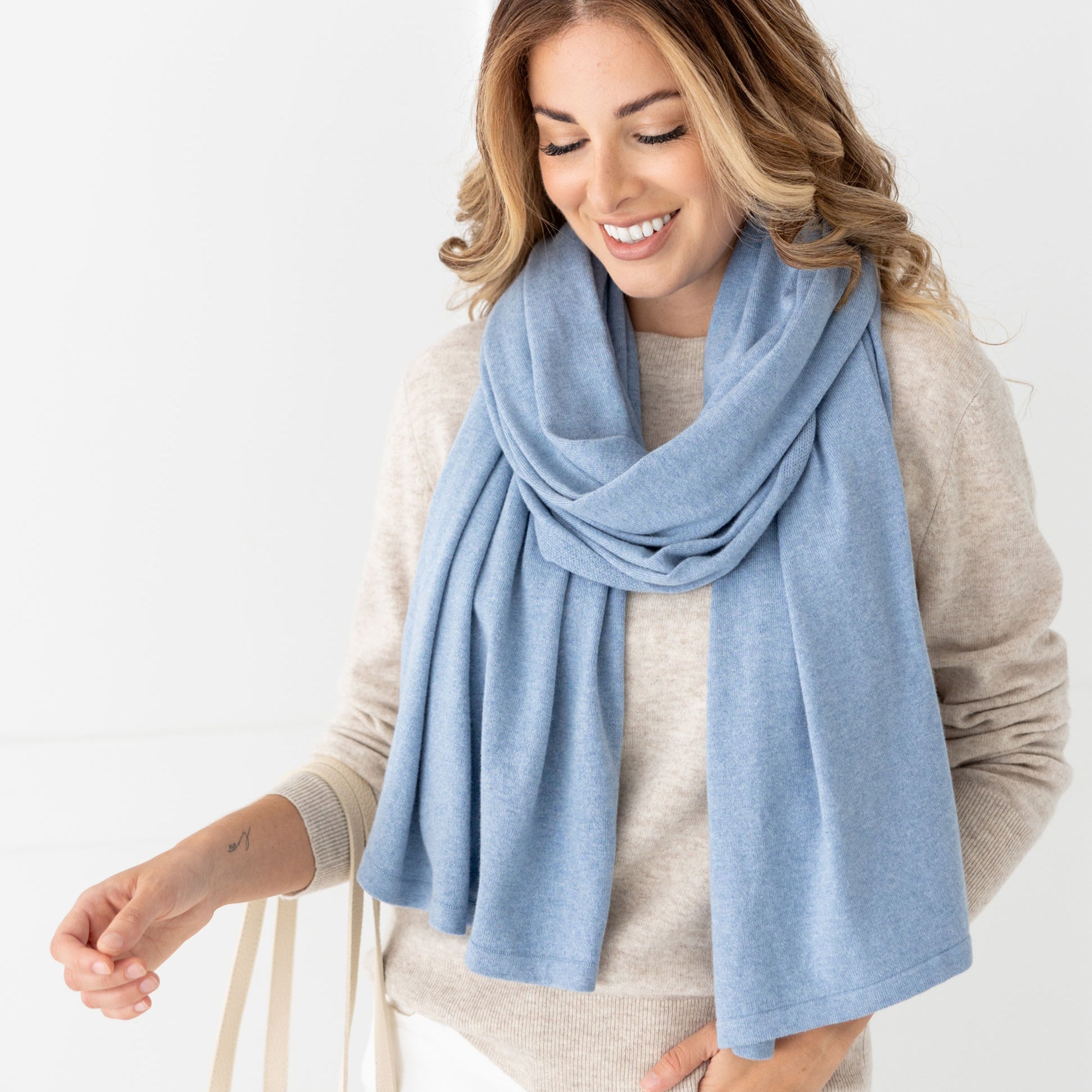 Woman wearing the Cashmere Cotton Luxe Travel Scarf in Horizon Blue which is a light blue scarf, wearing in a modern loop style